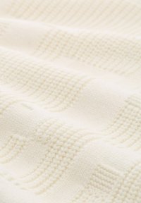 Strickdecke in Creme, die mit strukturierten Mustern aus erhöhten und flachen Stichen versehen ist und eine weiche, warme Oberfläche mit einem subtilen, eleganten Design schafft.
