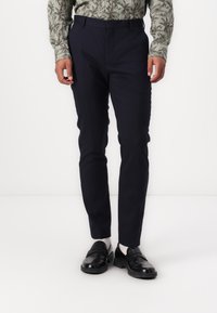 Marineblå slim-fit bukser lavet af glat stof, med en flad frontdesign og bæltestropper. Sammen med sorte loafers og lyse sokker.
