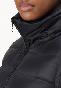 Close-up of a person wearing a black puffer jacket with a high collar zipped up near the chin, showing smooth fabric texture.