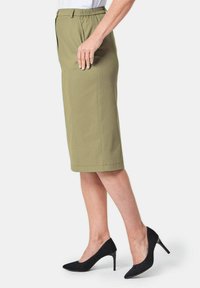 Olivgrüner knielanger Rock mit elastischem Bund, geradem Schnitt, seitlichen Taschen und kombiniert mit schwarzen spitzen Pumps.
