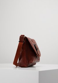 Bruine leren schoudertas met een zijflap, verstelbare schouderband en zilverkleurige hardware. Getextureerde afwerking met een subtiele glans.