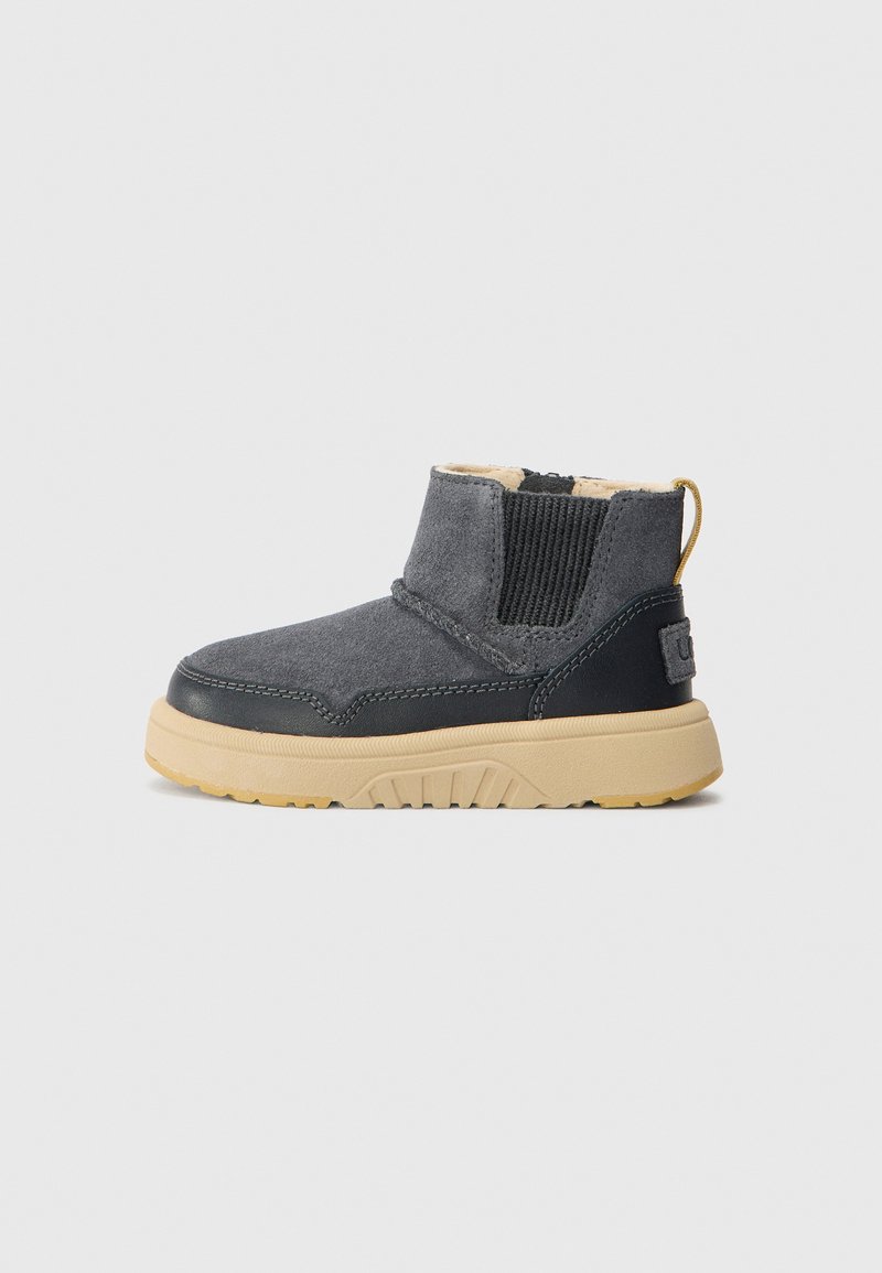Ankle boot in gray suede with a black leather base, elastic side panels, and a tan rubber sole. Features a pull tab at the back.