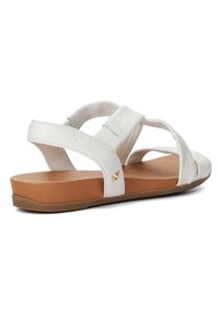 White leather sandal with cross straps, flat sole, and brown insole. Features a small gold accent on the side. Textured finish on straps.