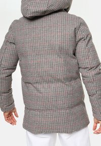 Toppatakki, jossa harmaa ja punainen tikattu neliökuosi, huppu, pulleat muodot, resorit hihansuissa ja hieman pidennetty selkäosa.