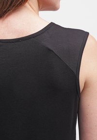 Gros plan sur le haut du dos d’une personne portant un haut noir sans manches avec des coutures visibles sur l’épaule et l’encolure.