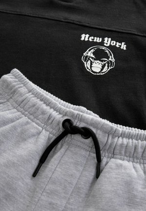 Camiseta negra con el texto "Nueva York" y un gráfico de gorila, combinada con pantalones de chándal grises que cuentan con una cinturilla elástica y un cordón negro.