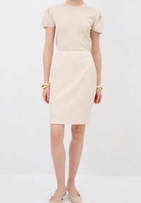 Vestido beige con mangas cortas y abullonadas, un torso ajustado y una falda lápiz hasta la rodilla. Textura suave, diseño minimalista, silueta elegante.