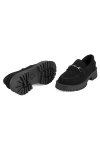Zwarte suede loafers met een chunky rubberen zool, voorzien van een decoratieve zilveren kettingaccent en geweven stikdetails.