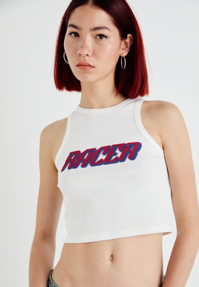 Hvit ribbestrikket crop topp med rund hals, som har "RACER" i fet rød og blå skrift over fronten. Glatt stofftekstur.