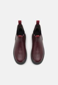 Burgundyfärgade läderankelstövlar med svarta gummisulor, elastiska sidoinlägg och dragflikar för enkel påtagning. Slät yta med minimala sömmar.