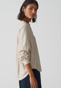 Beige langärmelig top met een ronde halslijn, relaxed fit en geplooide manchetten. Kenmerkt zich door een ronde zoom en lichtgewicht stof.