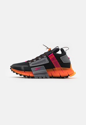 Black and orange athletic shoe with pink accents, thick segmented sole, grey overlays, and lace lock against white background.