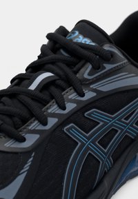 Scarpa sportiva nera con tomaia in mesh testurizzato, dettagli blu, lacci gommati e elementi di design stratificati. Presenta una suola ammortizzata.