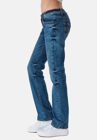 Pantalones vaqueros de mezclilla azul oscuro con corte slim, cinco bolsillos, cierre de botón y un ligero desvanecimiento. La tela muestra un ligero desgaste para un look casual.