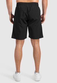 Pantalones cortos atléticos negros con cintura elástica, corte de longitud media y textura suave. Llevados con zapatillas blancas que tienen detalles en negro.