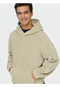 Beżowa bluza z polaru z kieszenią typu kangur, teksturowanym materiałem, luźnym fasonem i kapturem ze sznurkiem. Delikatne logo z przodu.