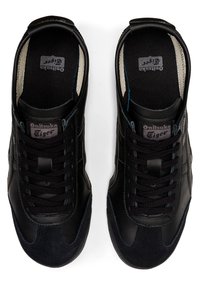 Black leather sneakers with a textured surface, featuring dark suede accents, black laces, and a logo label on the tongue.