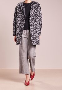Abrigo de leopardo gris con textura suave, mangas largas y cuello de solapa, combinado con pantalones de cuadros grises de pierna ancha y tacones rojos de punta.
