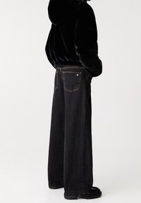 Black faux fur hoodie with elastic hem paired with high-waisted, wide-leg black denim jeans featuring two back pockets and gold stitching.