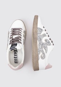 Baskets blanches avec des accents en paillettes argentées, lacets gris et semelle texturée beige. Présente un talon rose et un motif stylisé sur le côté.