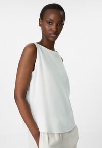 Haut sans manches bleu clair avec un col bateau, fabriqué dans un tissu texturé, présentant une coupe ample et de légentes fentes latérales pour plus de confort.