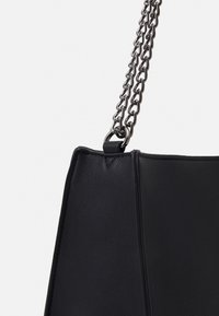 Černá kožená kabelka s texturovaným povrchem, vybavená stříbrným řetízkem a úhlovým tvarem, která se vyznačuje čistým, minimalistickým designem.