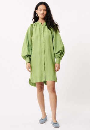Robe verte à manches ballons, confectionnée en tissu léger ; dotée d'un col mandarin et d'un ourlet arrondi. Portée avec des ballerines bleues.