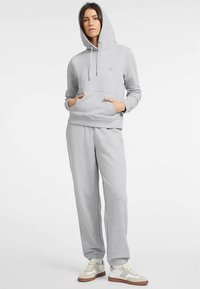 Sweat à capuche gris avec poche avant, cordon de serrage et ourlet côtelé, associé à un pantalon de survêtement gris assorti avec des poignets élastiques. Des chaussures décontractées complètent le look.