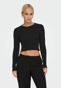 Top lungo a maniche lunghe a coste nere, con scollatura rotonda, abbinato a pantaloni neri a vita alta. Tessuto liscio e design aderente.