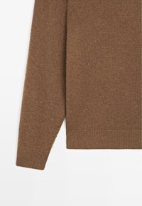 Hnědý pletený svetr s texturovaným povrchem, s ribbovaným lemováním a manžetami. Tkanina vypadá měkce a má teplý odstín.