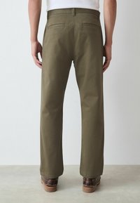Pantalones verde oliva en diseño de pierna recta, confeccionados en algodón, con dos bolsillos traseros y una textura suave, con costuras visibles.