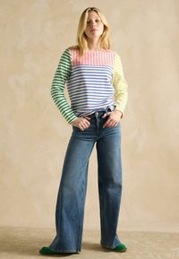 Mitmevärviline triibuline pika varruka pluus, kus on roosa, sinine, roheline ja kollane osa; kõrge vöökoht, laiad denim püksid; rohelised jalatsid.