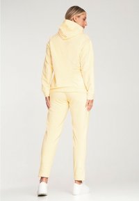 Jasnożółty dres składający się z bluzy z kapturem o długich rękawach i zwężających się spodni, wykonany z miękkiego materiału, dopełniony białymi sneakerami.