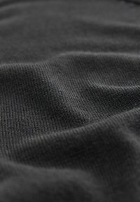 Gros plan sur un tissu gris foncé avec une surface texturée, montrant des plis doux et ondulés ainsi que des détails de tricot fins.