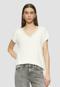 Weißes, kurzärmeliges V-Ausschnitt-T-Shirt mit Spitze am Ausschnitt, aus weichem Stoff und in bequemer Passform, kombiniert mit grauen hochgeschnittenen Jeans.