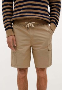 Beige cargo shorts lavet af letvægtsstof, med sidelommer, snøre i taljen og en afslappet pasform med glat tekstur.