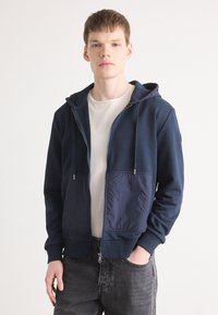 Navy zip-up hoodie with a soft fabric, featuring a smooth texture, adjustable drawstring hood, and a contrasting blue front pocket.