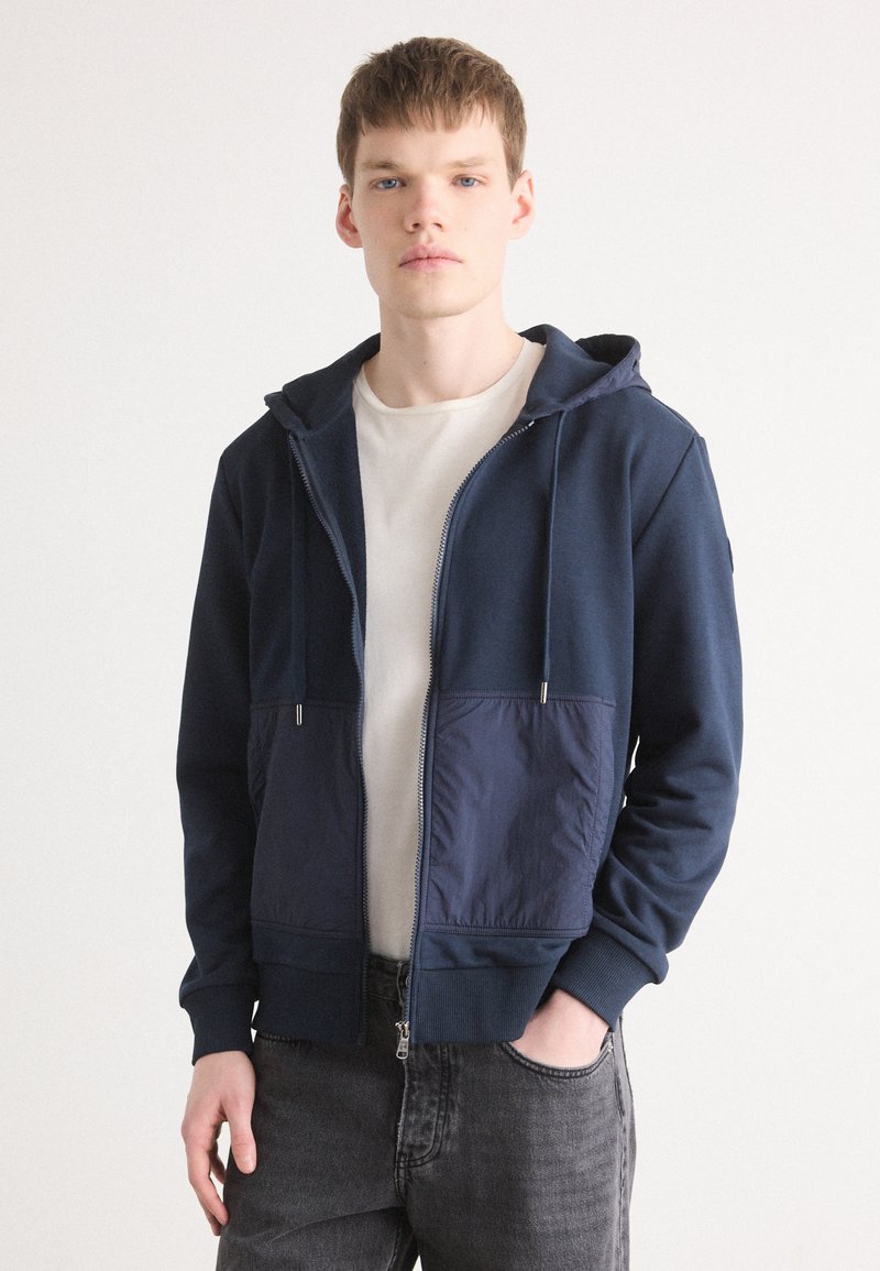 Navy zip-up hoodie with a soft fabric, featuring a smooth texture, adjustable drawstring hood, and a contrasting blue front pocket.
