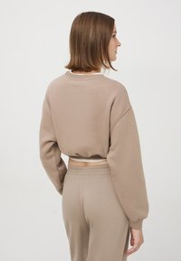 Skrojony beżowy sweter z oversize'owymi rękawami, ściągaczami oraz luźnym krojem, w zestawie z dopasowanymi beżowymi spodniami. Gładka tekstura.