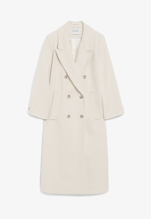 Dvostruki kaput u krem boji ima izrezanu reveru, bočne džepove i tipke kao akcent. Izrađen je od mekog materijala s oblikovanom siluetom.