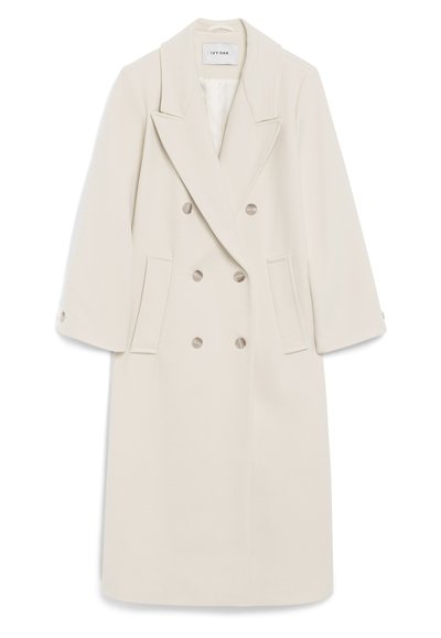 Double-breasted cream coat features a notched lapel, side pockets, and button accents. Made of soft fabric with a structured silhouette.