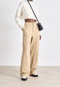 Beige wide-leg trousers with front pockets, paired with a cropped white sweater and cream platform shoes. Small black crossbody bag.