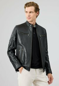 Zwarte leren jas met opstaande kraag, twee ritsborstzakken en twee zijventilaties. Gladde textuur en slim fit ontwerp.