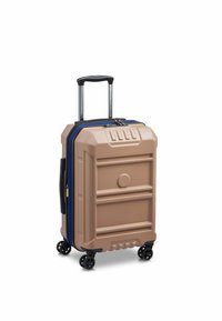 Valigia rigida di colore beige con finitura testurizzata, zipper blu, manico retrattile e quattro ruote nere per la mobilità.