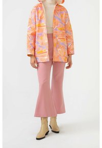 Regnjakke med blomsterprint i pink, orange og lavendel, kombineret med lyserøde vidde bukser og beige ankelstøvler.