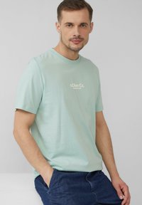Jasno miętowa bawełniana koszulka z krótkim rękawem i okrągłym dekoltem, z małym białym logo na obszarze klatki piersiowej. Luźny krój.