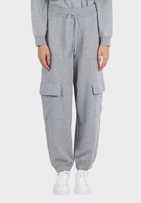 Pantaloni cargo jogger grigi a maglia con polsini elasticizzati, vita con coulisse, grandi tasche laterali, indossati con sneakers bianche con lacci.