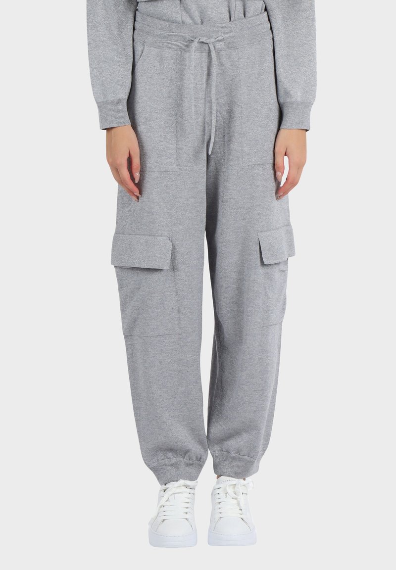 Pantaloni cargo jogger grigi a maglia con polsini elasticizzati, vita con coulisse, grandi tasche laterali, indossati con sneakers bianche con lacci.