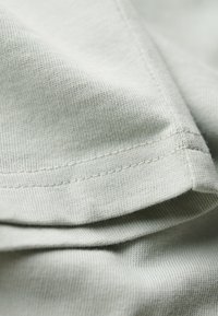 Tejido gris claro con una textura suave, que presenta una costura bien cosida. El material exhibe un patrón de punto fino y un leve brillo.