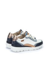 Zapatilla de cuero con una combinación de colores blanca, marino y beige. Presenta un acabado texturizado, lengüeta acolchada y un acento metálico en el talón.